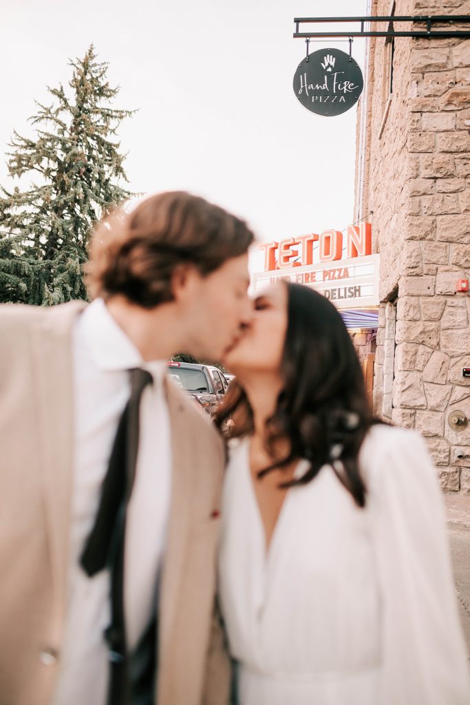 bride and groom kissing in jackson hole in front of teton pizza taken by adrian wayment photo