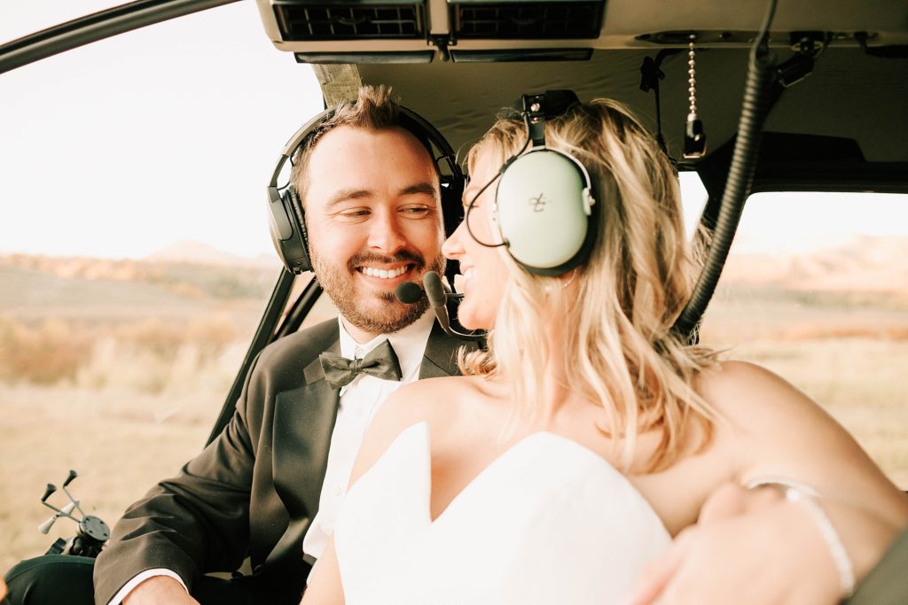 bride and groom in the helicopter with their head sets on, smiling at each other before take off.