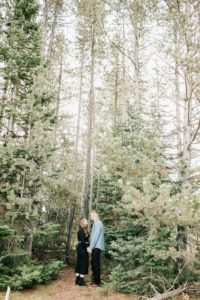 engaged couple holding hands facing each other in the pine trees in grand teton national park taken by adrian wayment photo.