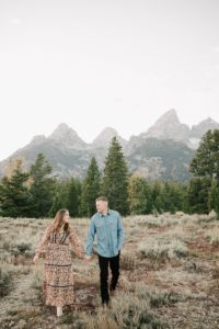 engaged couple in grand teton national park holding hands walking together.