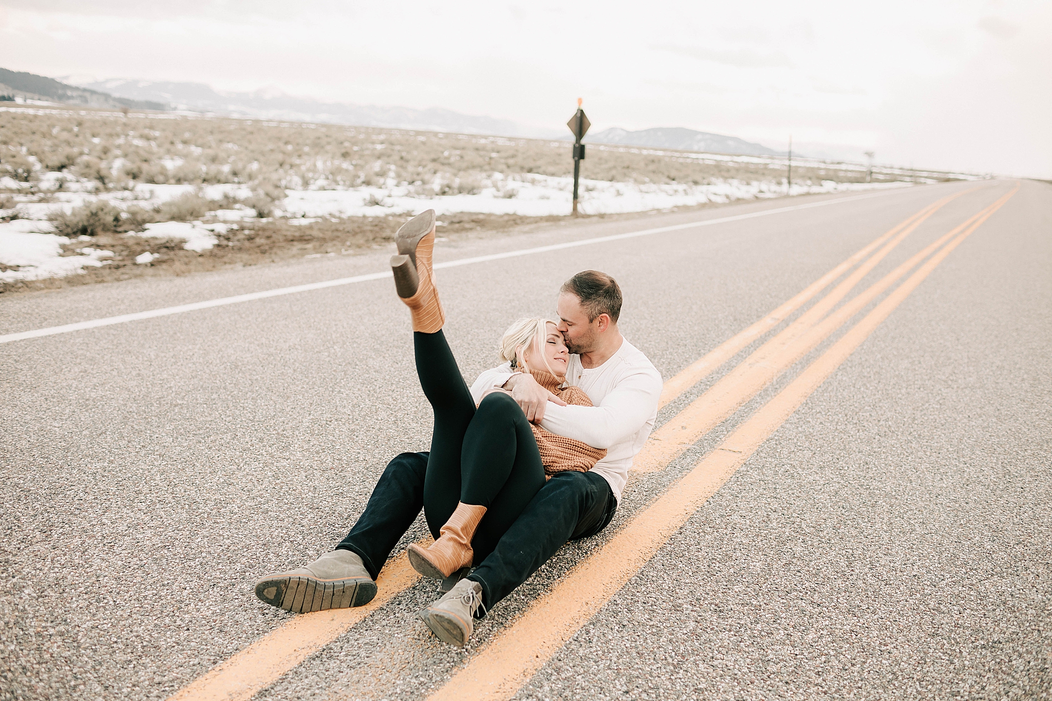 engaged boy and girl sitting on the road during their engagement session at the snake river overlook.