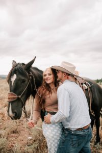 boy kissing girl on the cheek as they stand next to their horse during their western engagement photoshoot taken by photographer adrian wayment photo.