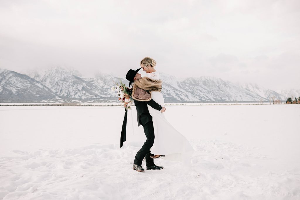 groom holding bride in the snow at their jackson hole destination wedding in grand teton national park in the winter.